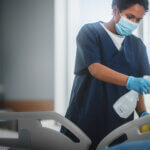 A healthcare professional sanitizes a hospital bed with a EN 14476 certified disinfectant, focusing intently on the task to ensure a clean and safe environment for patients.