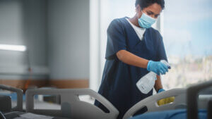 A healthcare professional sanitizes a hospital bed with a EN 14476 certified disinfectant, focusing intently on the task to ensure a clean and safe environment for patients.