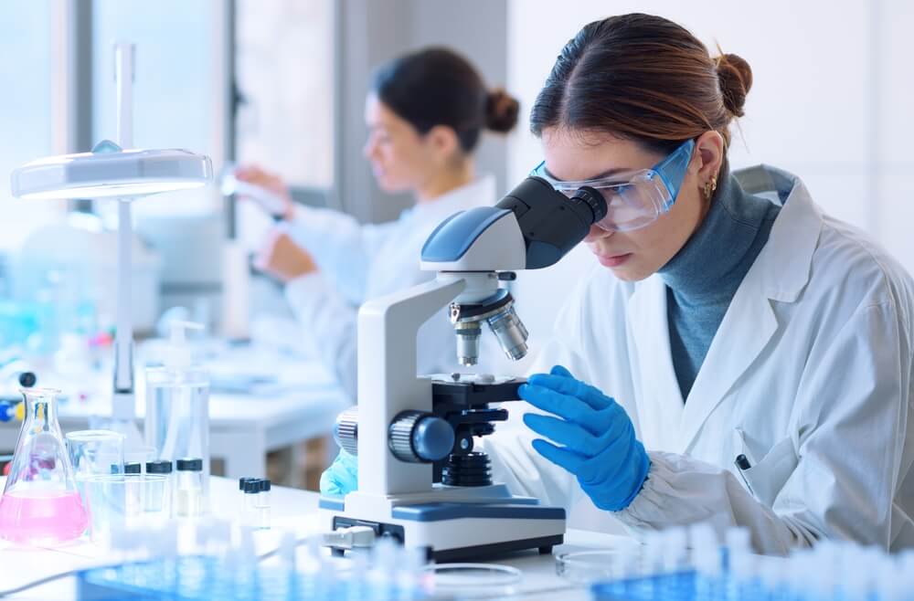 The image describes a lab technician performing biocidal product testing using a microscope to enumerate the viable spores.