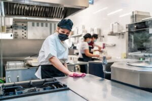 female cook disinfecting her kitchen after work in food service sector