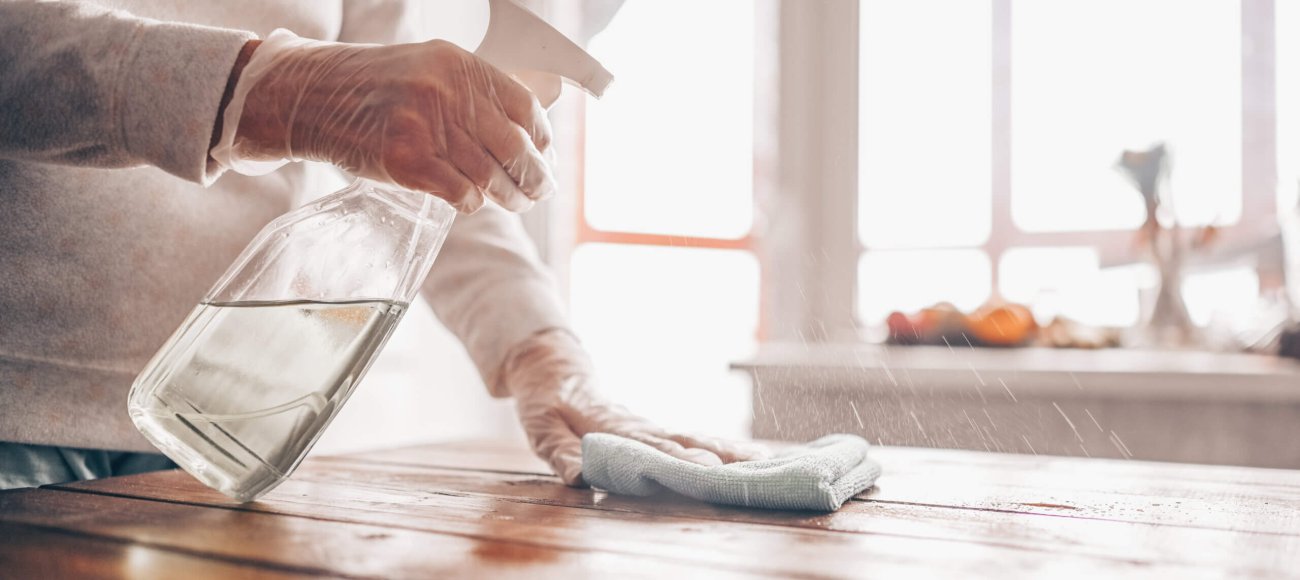 Image of a person using EN 14476 certified surface sanitizer to sanitize the table top