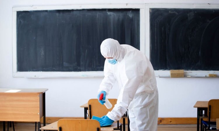The image depicts a person wearing a PPE and sanitizing the school using EN 14347 tested disinfectants.