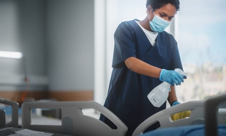 A healthcare professional sanitizes a hospital bed with a EN 14476 certified disinfectant, focusing intently on the task to ensure a clean and safe environment for patients.