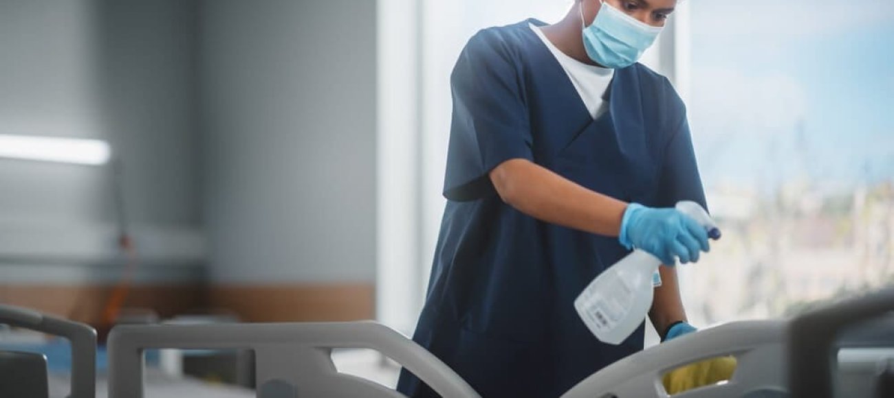 A healthcare professional sanitizes a hospital bed with a EN 14476 certified disinfectant, focusing intently on the task to ensure a clean and safe environment for patients.
