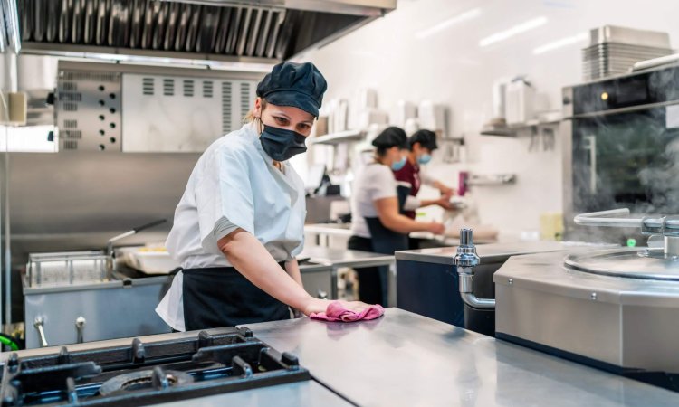 female cook disinfecting her kitchen after work in food service sector